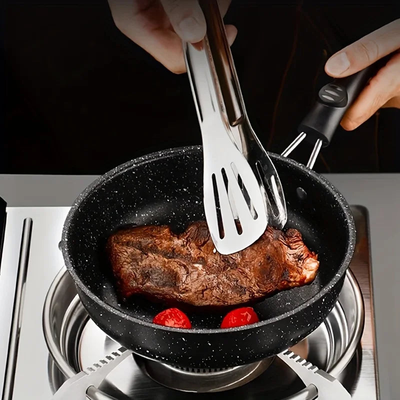 Compact cast iron skillet with speckled black finish cooking seared meat and tomatoes, metal spatula lifting food, stovetop s