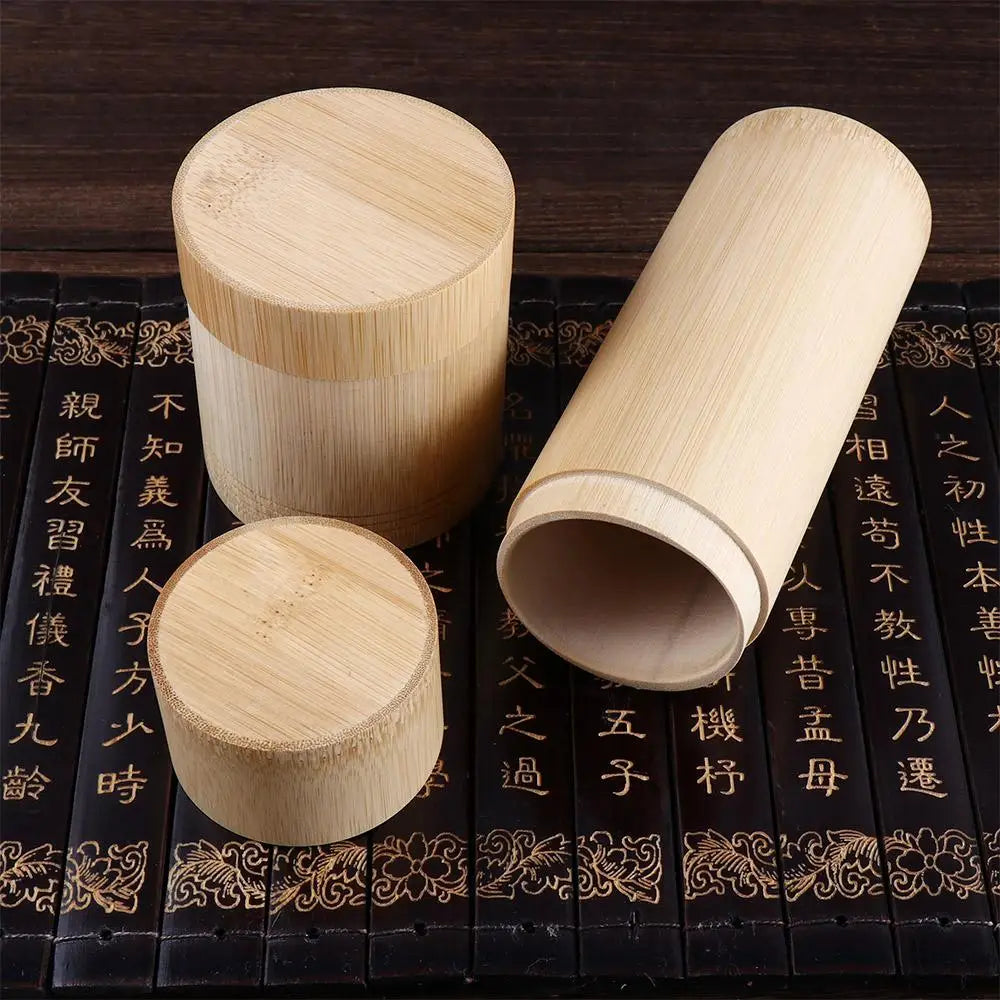 Three handcrafted bamboo tea storage canisters with lids displayed on decorative black surface with gold Asian characters.
