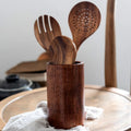 Wooden kitchen utensil set with spatula, slotted spoon, and fork in dark wood storage holder on kitchen counter