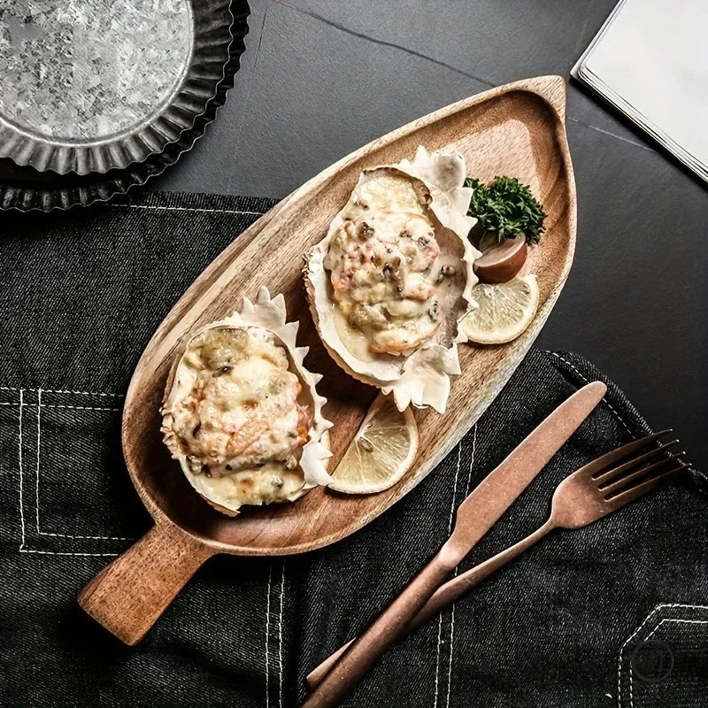 Palm leaf-shaped wooden serving tray with two oysters, lemon slices, and fresh herbs, displayed with copper utensils on dark 