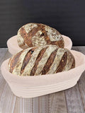 Two artisan sourdough loaves with scored crusts in a natural rattan proofing basket lined with cloth on wooden surface.
