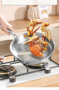 Pure titanium fry pan with crab and vegetables cooking on stovetop, showing natural non-stick surface and ergonomic handle.
