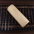 Handcrafted bamboo tea storage box with carved cylindrical design, displayed on antique Chinese books with gold lettering and