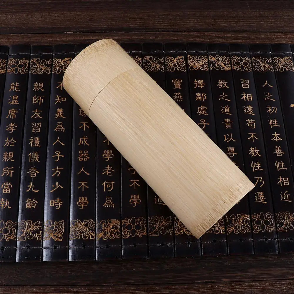 Handcrafted bamboo tea storage box with carved cylindrical design, displayed on antique Chinese books with gold lettering and