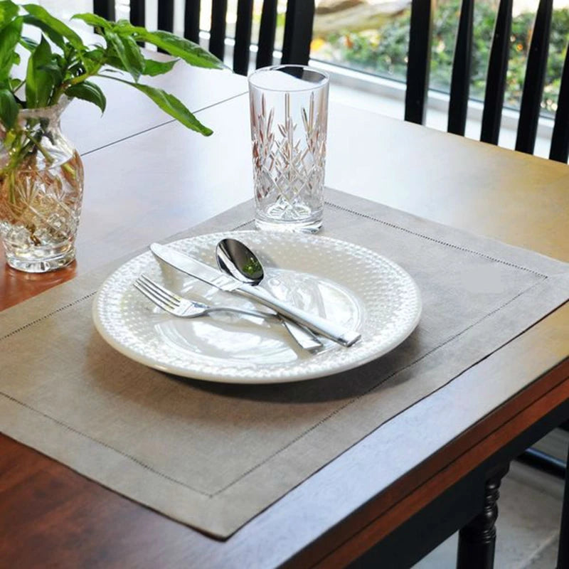 Natural linen placemat with hempstitched edges displayed on dining table with white plate, cutlery, and crystal glassware