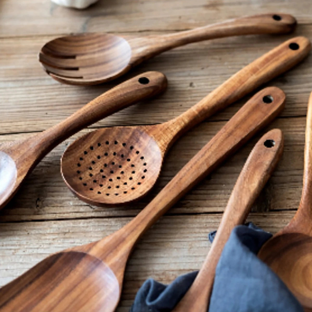 Wooden kitchen utensils set including spatula, slotted spoon, and fork displayed on wooden surface with natural grain detail.