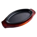 Cast iron oval griddle pan on wooden serving board with decorative rim, dark cooking surface visible.