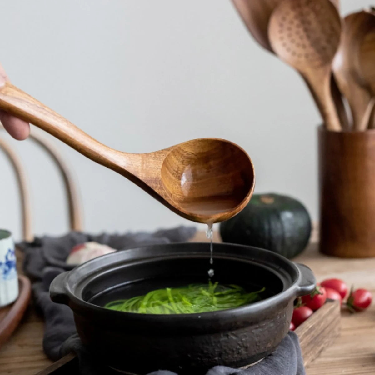 Wooden kitchen utensils dripping water into black ceramic bowl with green matcha, wooden utensil holder visible in background