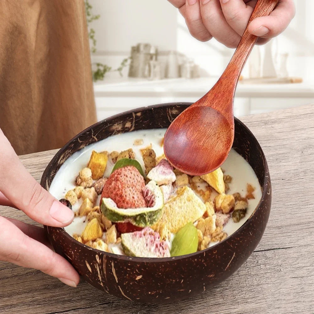 Handcrafted coconut bowl filled with granola, yogurt, and fresh fruits, held with wooden spoon