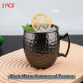 Black matte hammered copper mug with ice, lemon slice, and mint garnish on wooden coaster