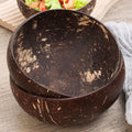 Natural coconut shell serving bowl with rustic texture, shown open displaying interior, paired with fresh salad in background