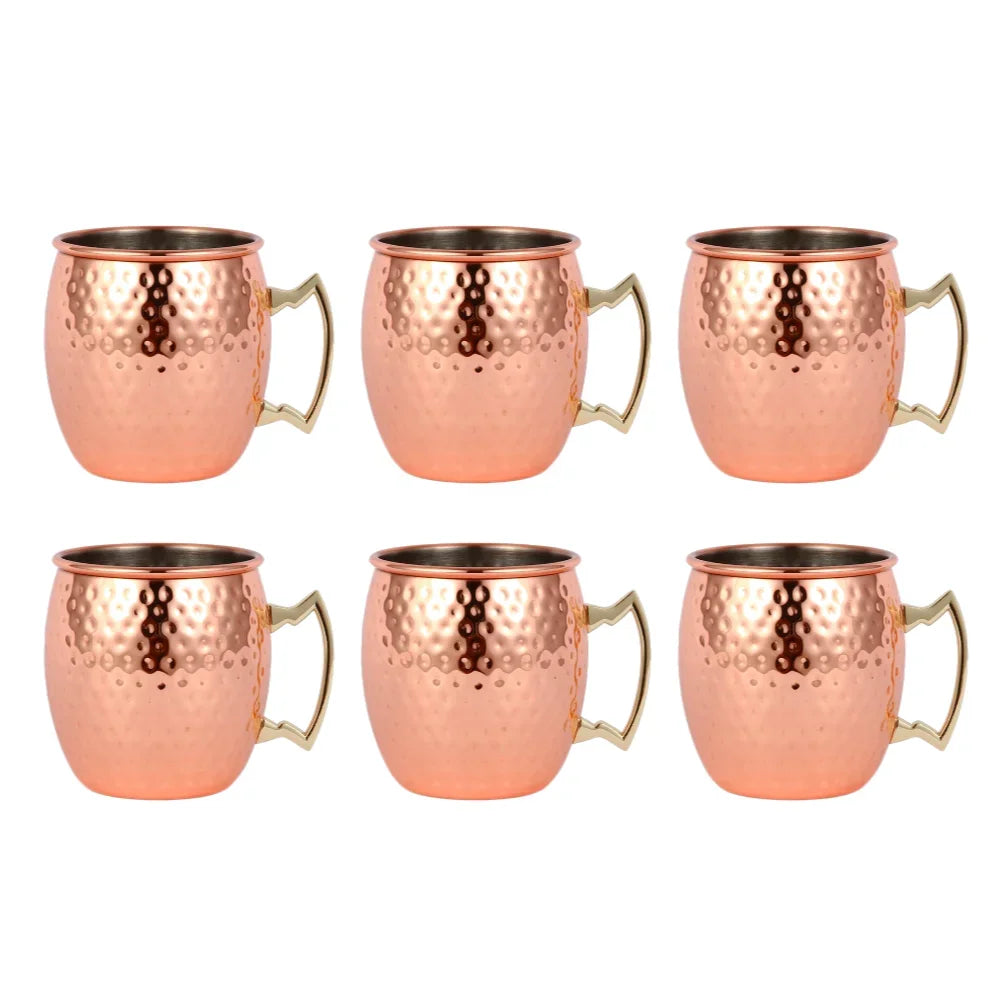 Set of 6 hammered copper Moscow mule mugs with brass handles and stainless steel interiors, arranged in two rows on white bac