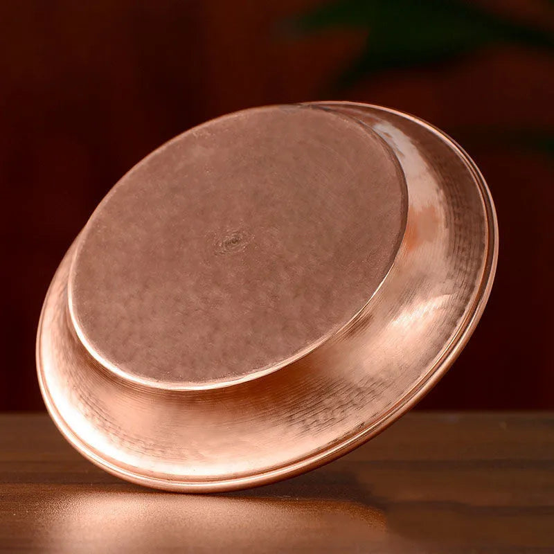 Polished copper serving plate tilted to show curved edges and reflective surface against warm background.