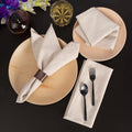 Beige cotton linen napkins styled on plates with black utensils, flowers, and glassware on dark background