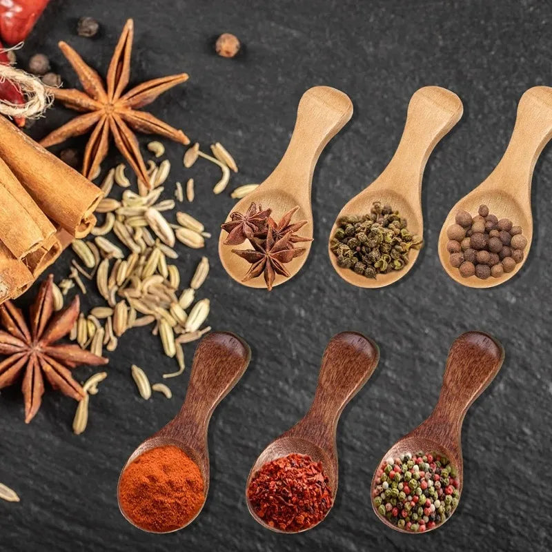 Bamboo mini scoop spoons with various spices and seasonings on dark slate, showcasing natural wood kitchen utensils for tea, 