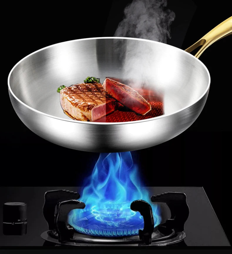 Stainless steel wok pan with golden handle cooking meat over blue flame, demonstrating heat distribution and non-stick surfac