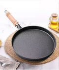 Cast iron egg skillet with wooden handle on cork mat, surrounded by olive oil bottle and kitchen linens on marble surface.