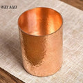 Handcrafted pure copper glass with hammered texture, polished interior, displayed on neutral fabric background.