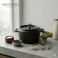 Cast iron Dutch oven with lid surrounded by wooden bowls, glass herb jar, ceramic pitcher, and fresh herbs on concrete surfac
