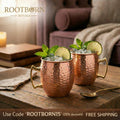 Hammered copper insulated travel cups with brass handles, lime slices and fresh mint garnish, on wooden table in cozy living 