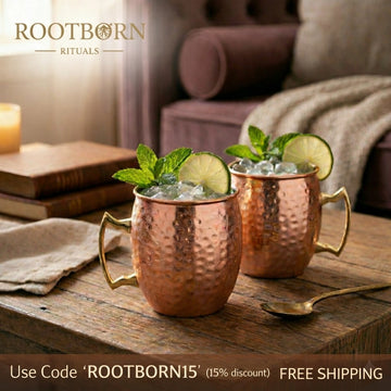 Hammered copper insulated travel cups with brass handles, lime slices and fresh mint garnish, on wooden table in cozy living 