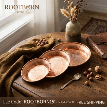 Three artisanal copper serving plates with hammered texture displayed on wooden table with dried flowers, nuts, and natural l